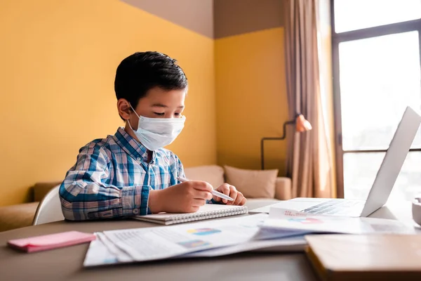 Ασιατικό Αγόρι Στην Ιατρική Μάσκα Γράφοντας Και Μελετώντας Στο Διαδίκτυο — Φωτογραφία Αρχείου