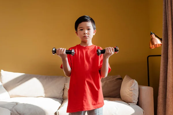 アジア系の少年が独居中にダンベルと一緒に家で運動する — ストック写真