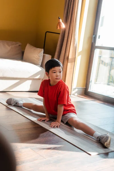 sportive asian boy in twine pose on fitness mat at home during quarantine
