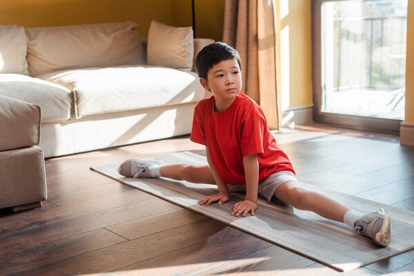 athletic asian boy in twine pose on fitness mat at home during quarantine