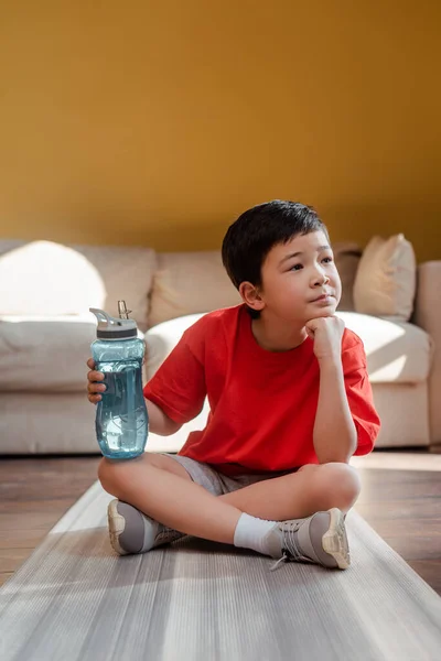 Thoughtful Sportive Asian Boy Sports Bottle Sitting Fitness Mat Home — Stock Photo, Image