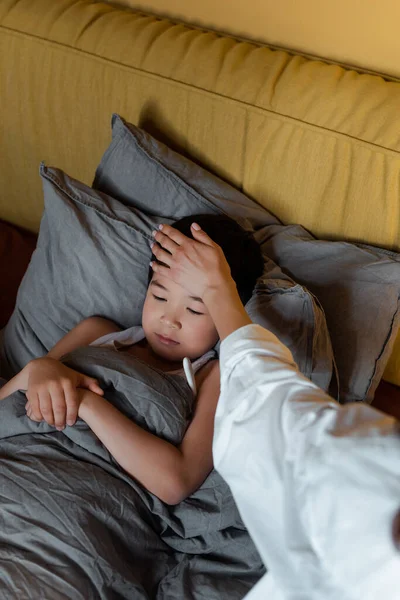 アジア系の少年は体温で隔離された母親とベッドに寝そべって — ストック写真