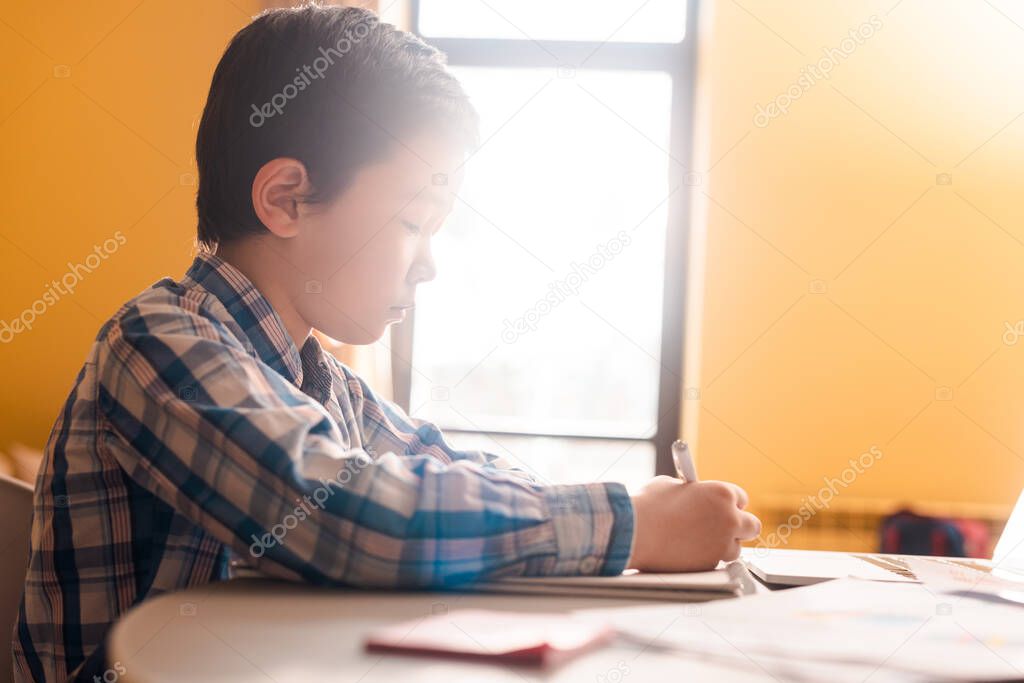 asian boy writing and studying at home with sunlight during quarantine