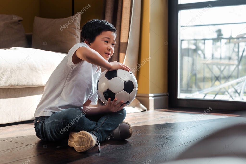 asian boy with football ball watching sports match at home on quarantine
