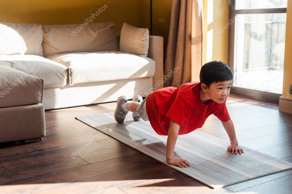 adorable sportive asian boy doing plank on fitness mat at home during self isolation