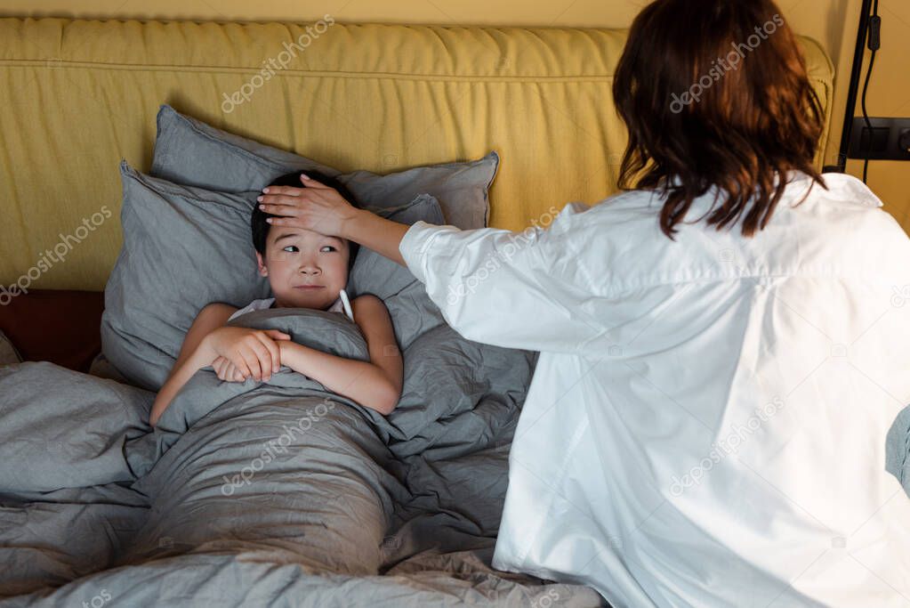 ill asian boy having fever and lying in bed with mother near on quarantine