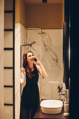 Siyah elbiseli mutlu kız akıllı telefondan konuşuyor ve elinde tıbbi maske var. Karantina sona erdi. 