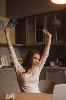 Dizüstü bilgisayarın yanında elinde spor biletleri olan heyecanlı bir kadının seçici odak noktası. Karantina konseptinin sonu.