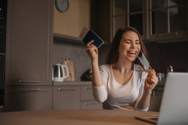 Medikal maskeli neşeli serbest çalışanın elinde pasaport, laptopun yanında uçak bileti, karantina konseptinin sonu.