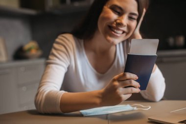 Tıbbi maskenin yanında pasaportu olan mutlu bir kadının seçici odak noktası, karantina konseptinin sonu.