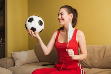 Mutlu sporcu kadın tıbbi maskeye dokunuyor ve elinde futbol topu tutuyor. Karantina sona erdi. 