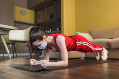 Spor maskeli ve spor kıyafetli bir kadın spor minderinde tahta örtü yapıyor. 
