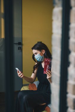 Tıbbi maskeli ve siyah elbiseli genç bir kadının gece parti biletleri bulundurması ve akıllı telefon kullanması, karantina konseptinin sonu. 