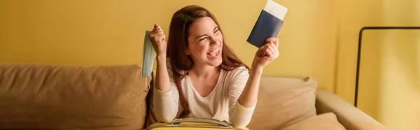 持有护照和机票的戴着医疗面具的快乐年轻女性的全景定位 检疫概念的终结 — 图库照片