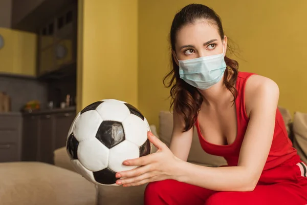 Αθλητική Γυναίκα Ιατρική Μάσκα Κρατώντας Ποδόσφαιρο Στο Σπίτι — Φωτογραφία Αρχείου