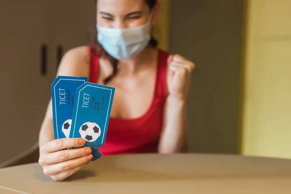 スポーツマッチチケットを保持する医療マスクの幸せな女性の選択的焦点 — ストック写真