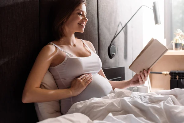Glücklich Schwangere Frau Liest Buch Und Berührt Bauch Schlafzimmer — Stockfoto