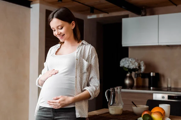 快乐而又怀孕的女人在饭桌边摸着肚子 — 图库照片