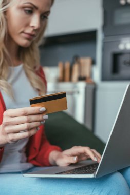 Kredi kartı tutarken dizüstü bilgisayar kullanan genç bir kadının seçici odak noktası