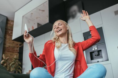 Kulaklıklı mutlu kadının düşük açılı görüntüsü. Akıllı telefonu tutarken gözleri kapalı şarkı söylüyor.