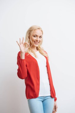 cheerful beautiful girl showing okay gesture while smiling at camera isolated on white clipart