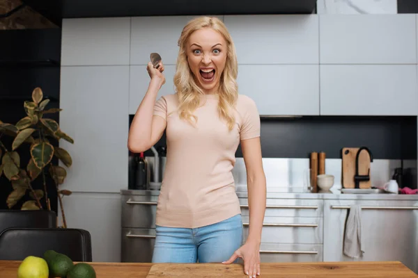 aggressive young woman holding knife and looking at camera while standing at table with fresh vegetables