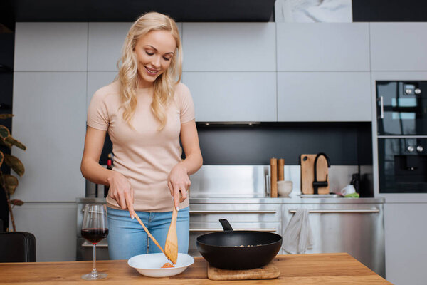 smiling woman putting thai noodles on plate with wooden spatulas