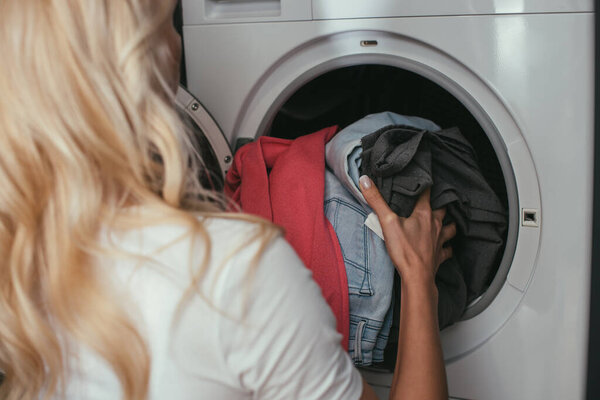 back view of housewife putting laundry into washing machine