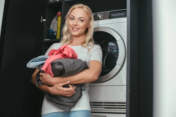 Çamaşır Makinesinin Yanında Çamaşır Makinesini Tutarken Kameraya Bakan Gülümseyen Kadınının — Stok fotoğraf