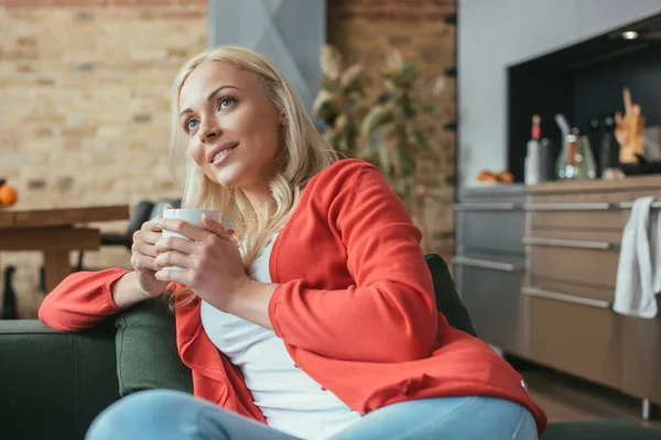 Gülümseyen Kadın Bir Fincan Çayla Kanepede Otururken Gözlerini Kaçırıyor — Stok fotoğraf