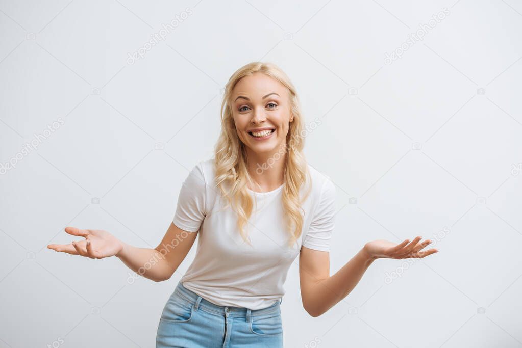 happy blonde woman smiling at camera while standing with open arms isolated on white