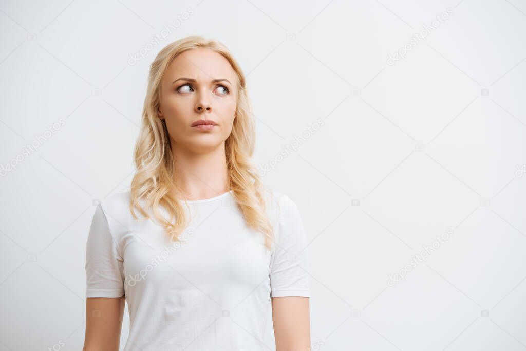 thoughtful blonde woman looking away while standing isolated on white