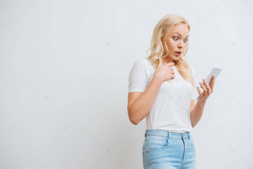 shocked girl holding hand on chest during video chat on smartphone isolated on white