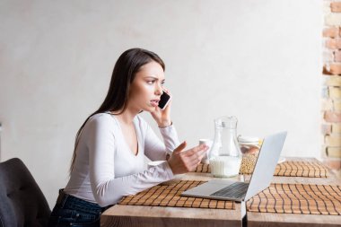 üzgün serbest çalışan bilgisayarın yanında akıllı telefondan konuşuyor ve sütle dolu sürahi 