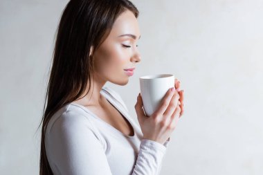 Bir fincan çay tutan, gözleri kapalı bir kadının yan görüntüsü. 