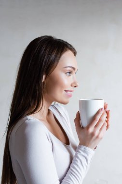 Elinde bir fincan çay tutan ve evinde gülümseyen neşeli kadının yan görüntüsü. 