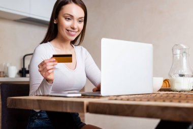 Bilgisayarın ve akıllı telefonun yanında kredi kartı tutan mutlu kızın seçici odak noktası. 