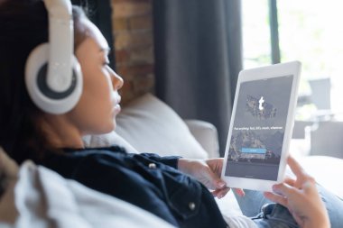 KYIV, UKRAINE - 29 Nisan 2020: Kablosuz kulaklıklı kız müzik dinliyor ve tumblr uygulamalı dijital tablet kullanıyor 