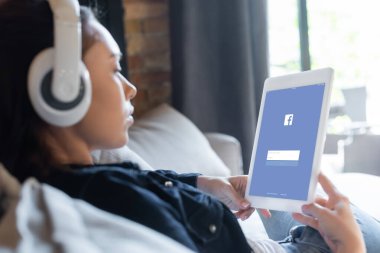 KYIV, UKRAINE - 29 Nisan 2020: kablosuz kulaklık takan, müzik dinleyen ve facebook uygulamalı dijital tablet kullanan kız odaklı 
