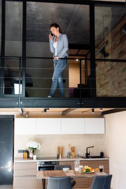 Dublex apartmanın ikinci katında dururken akıllı telefondan konuşan genç bir kadın. 
