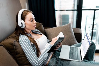 KYIV, UKRAINE - 29 Nisan 2020: Kablosuz kulaklıklı çekici bir kadın dizüstü bilgisayara facebook web sitesi ve online çalışma konsepti ile birlikte yazıyor. 