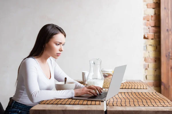 Bellissimo Freelance Con Computer Portatile Vicino Brocca Con Latte Ciotola — Foto Stock