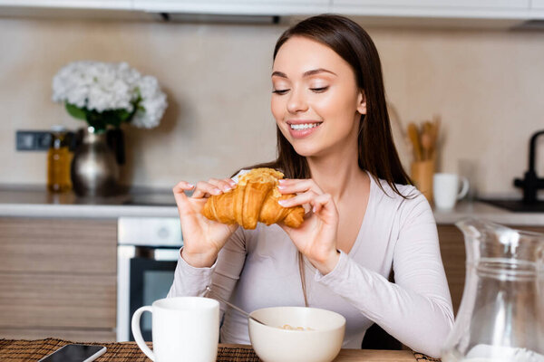 happy girl holding tasty croissant near bowl and cup 