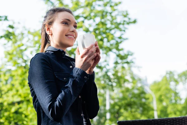 Szczęśliwa Młoda Kobieta Dżinsowej Kurtce Trzyma Filiżankę Kawy Zewnątrz — Zdjęcie stockowe