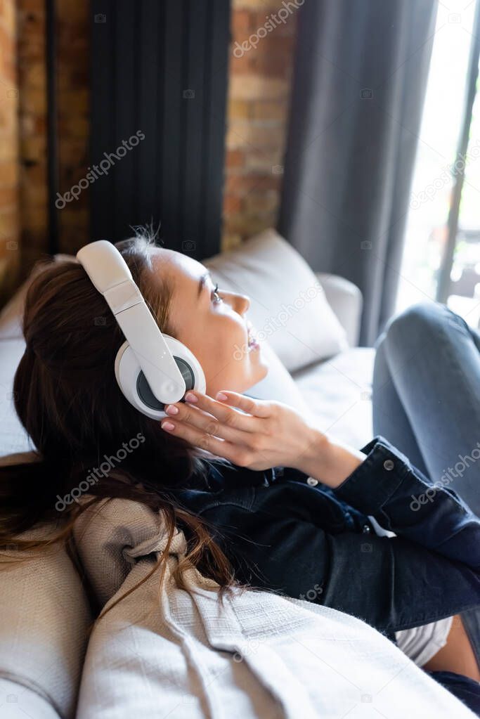 side view of cheerful girl touching wireless headphones while listening music 