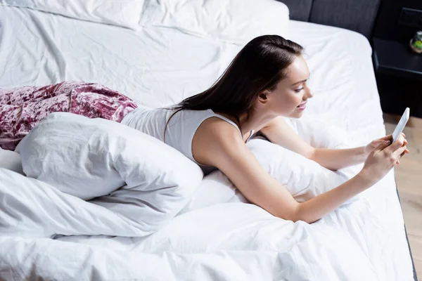 Feliz Jovem Mulher Usando Smartphone Enquanto Deitado Cama — Fotografia de Stock
