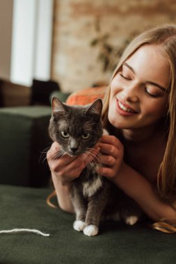 Mutlu genç kadın oturma odasında sevimli kediye dokunuyor.