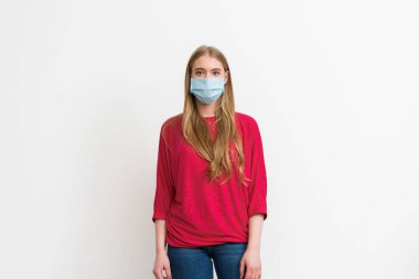 Tıbbi maskeli genç bir kadın beyazların üzerinde tek başına duruyor. 