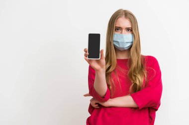 Medikal maskeli kadın elinde beyaz ekranlı akıllı telefon tutuyor. 