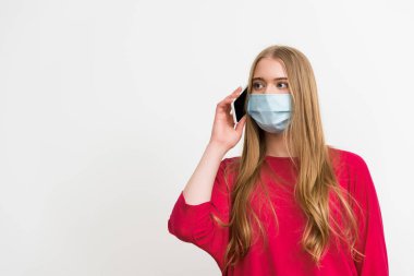Medikal maskeli genç bir kadın beyaz telefondan izole edilmiş bir şekilde konuşuyor. 
